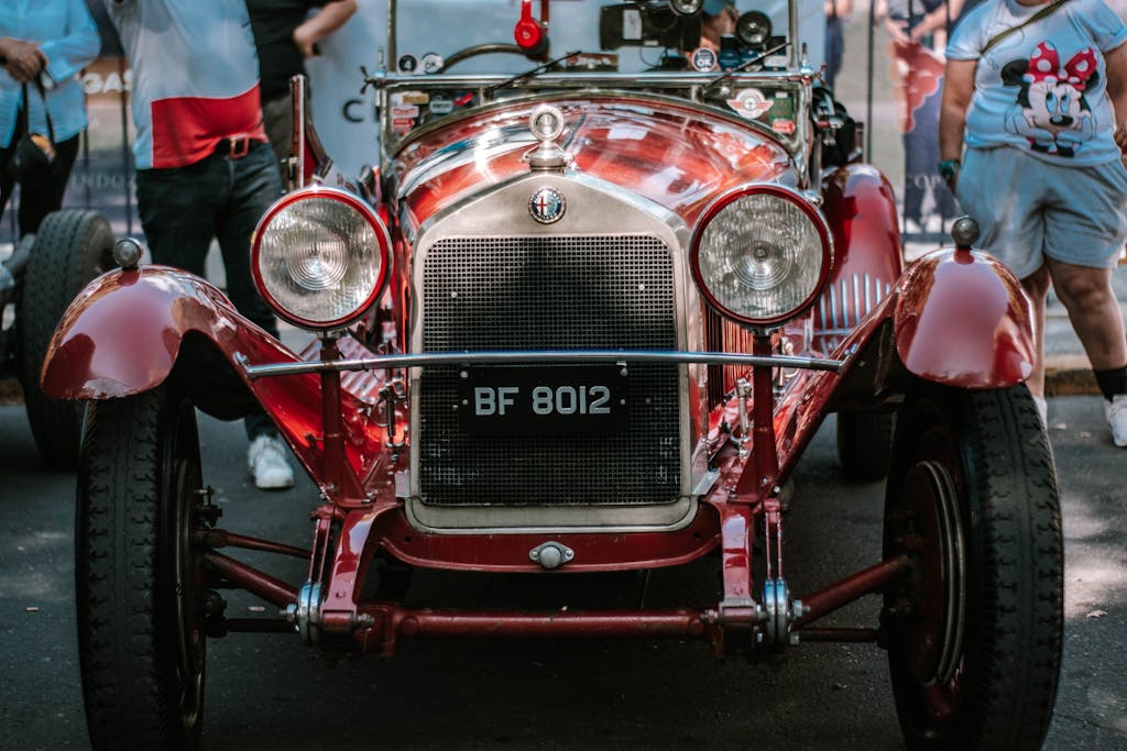 A vintage car is parked in front of people